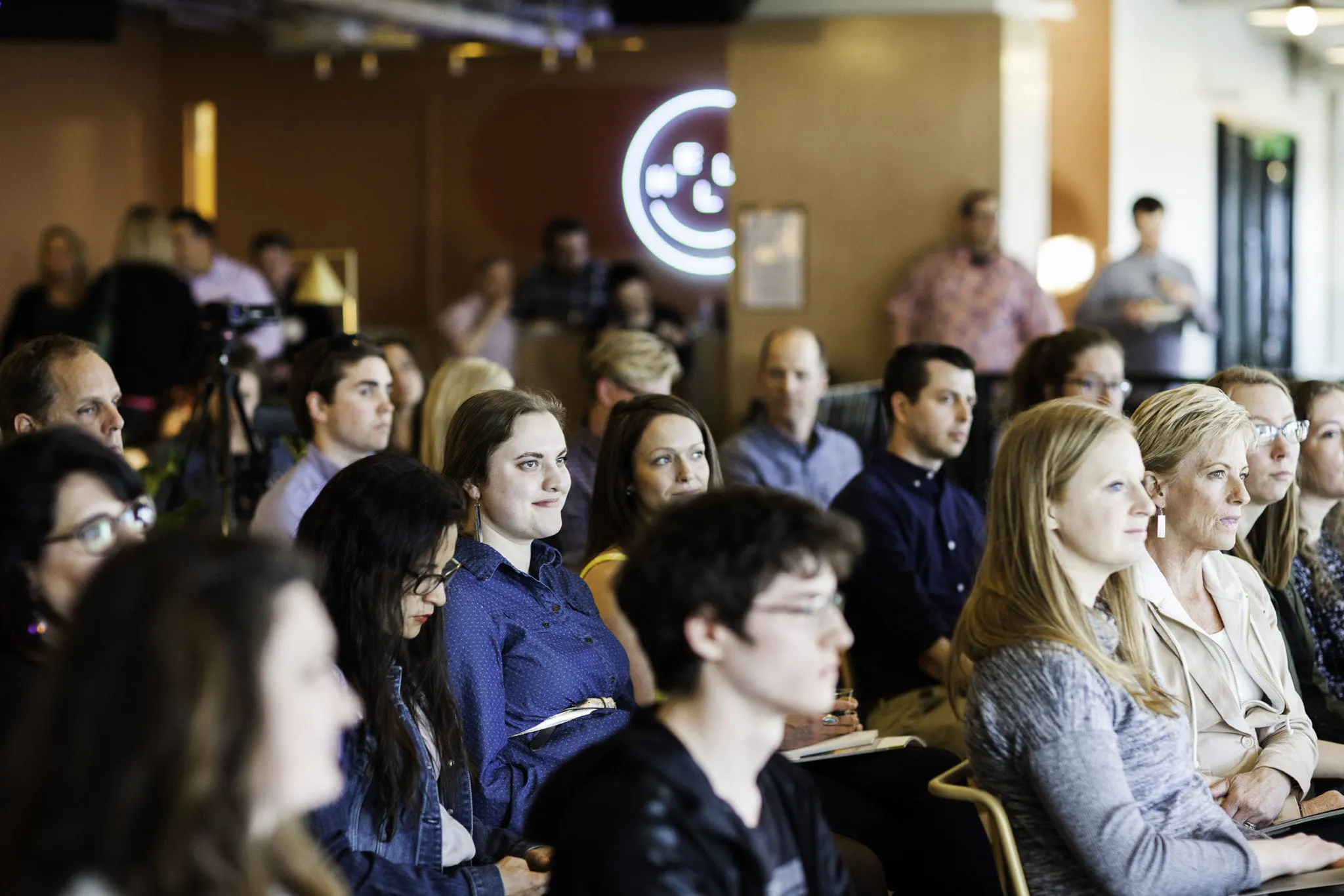 A group of audience members sitting in rows watching a presentation.