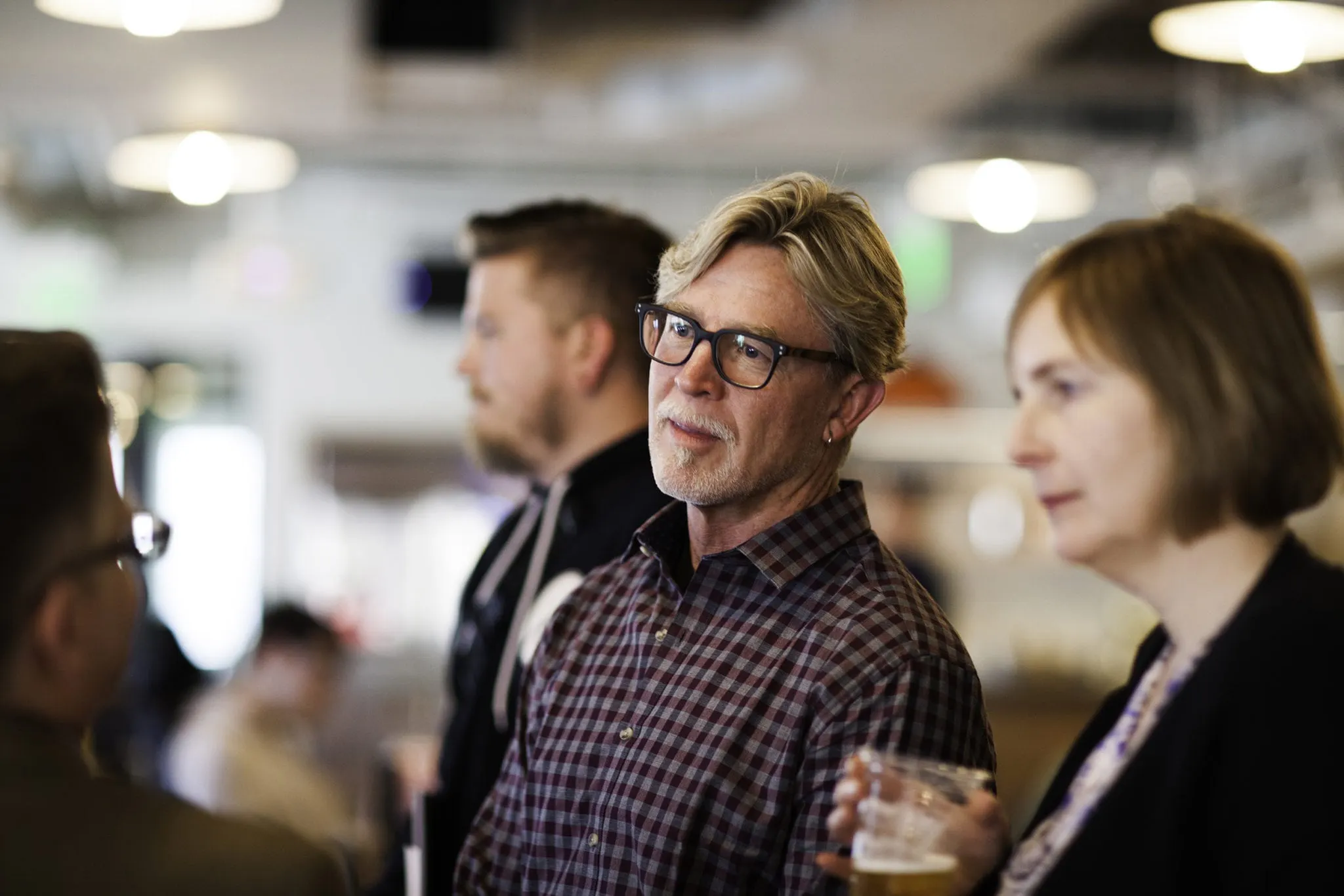 Two men and a woman standing in an audience listening to a speaker at a presentation.