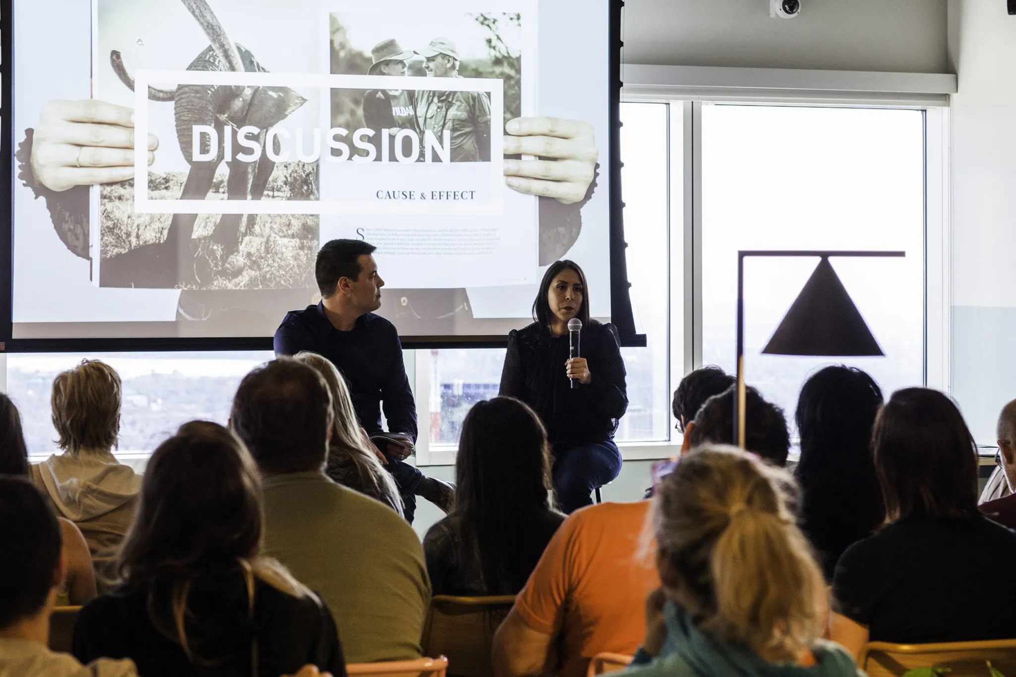 A man and a woman holding microphones and speaking to an audience during a presentation.