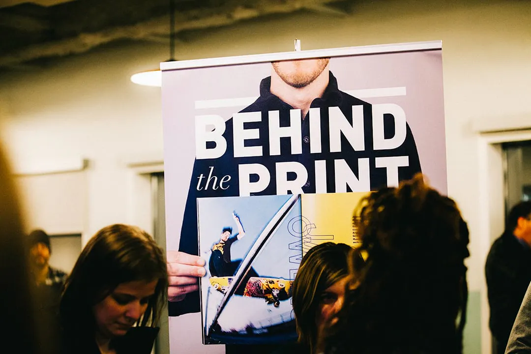 Three people standing in front of a custom banner printed with Behind the Print in white.
