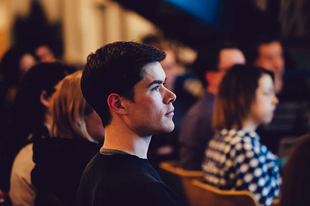 A man sitting in an audience with other people sitting around him during a presentation.