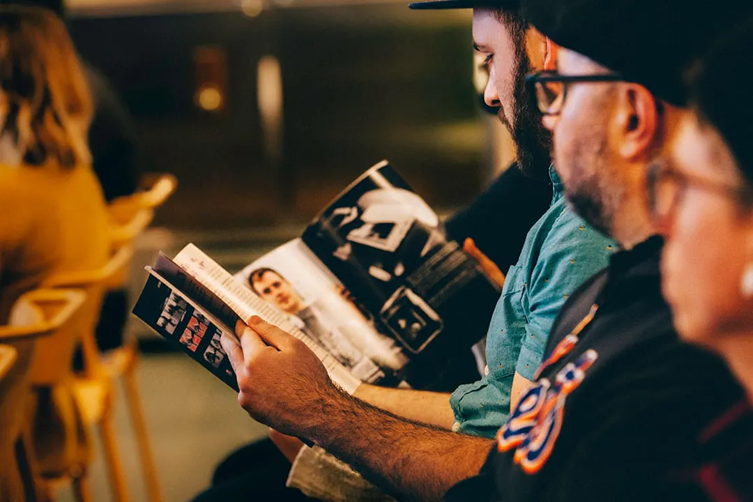 Two men sitting in an audience flipping through a custom printed magazine.
