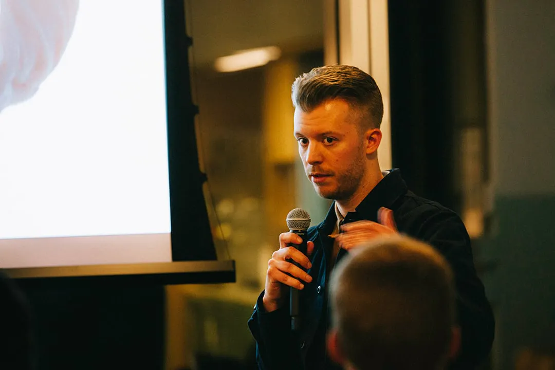 A man speaking in front of an audience with a microphone during a presentation.