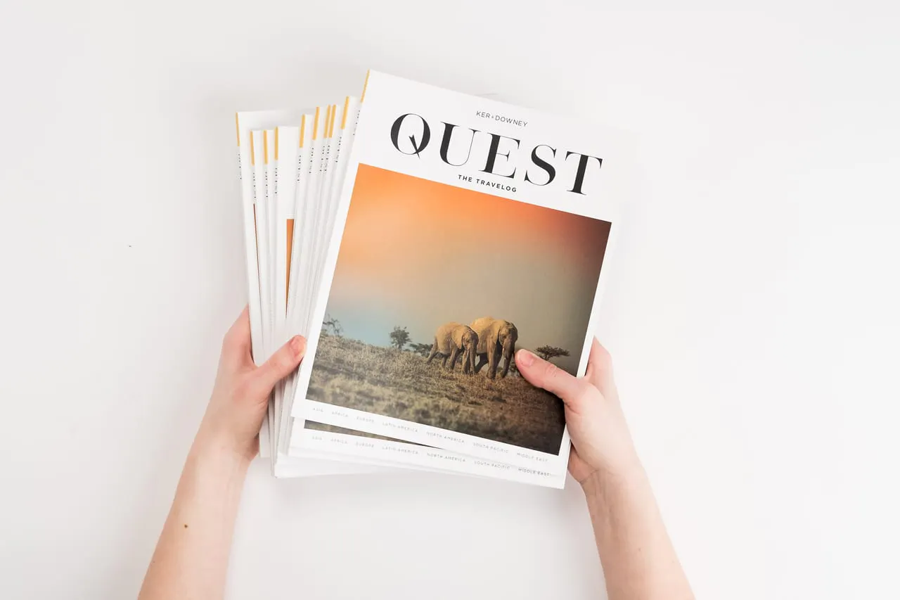 Two hands holding a fanned-out stack of Quest travel books printed with elephants on the cover.