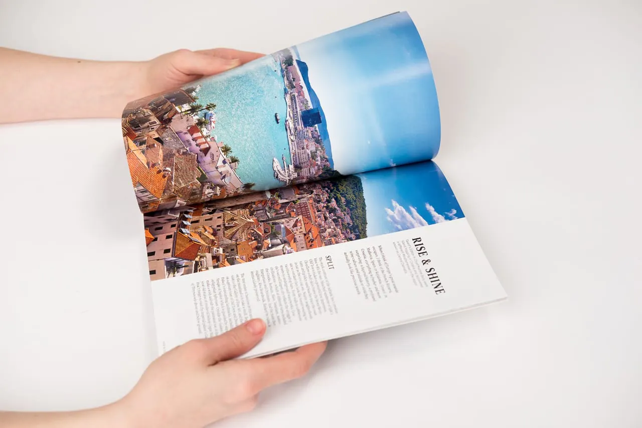 Two hands holding a travel book open to images of a European city on the water and Rise & Shine in black.