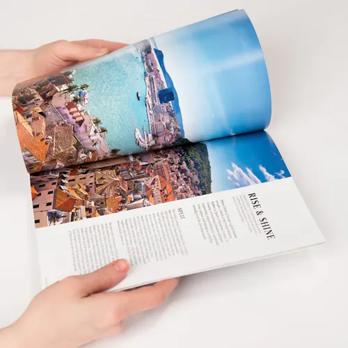 Two hands holding a travel book open to images of a European city on the water and Rise & Shine in black.
