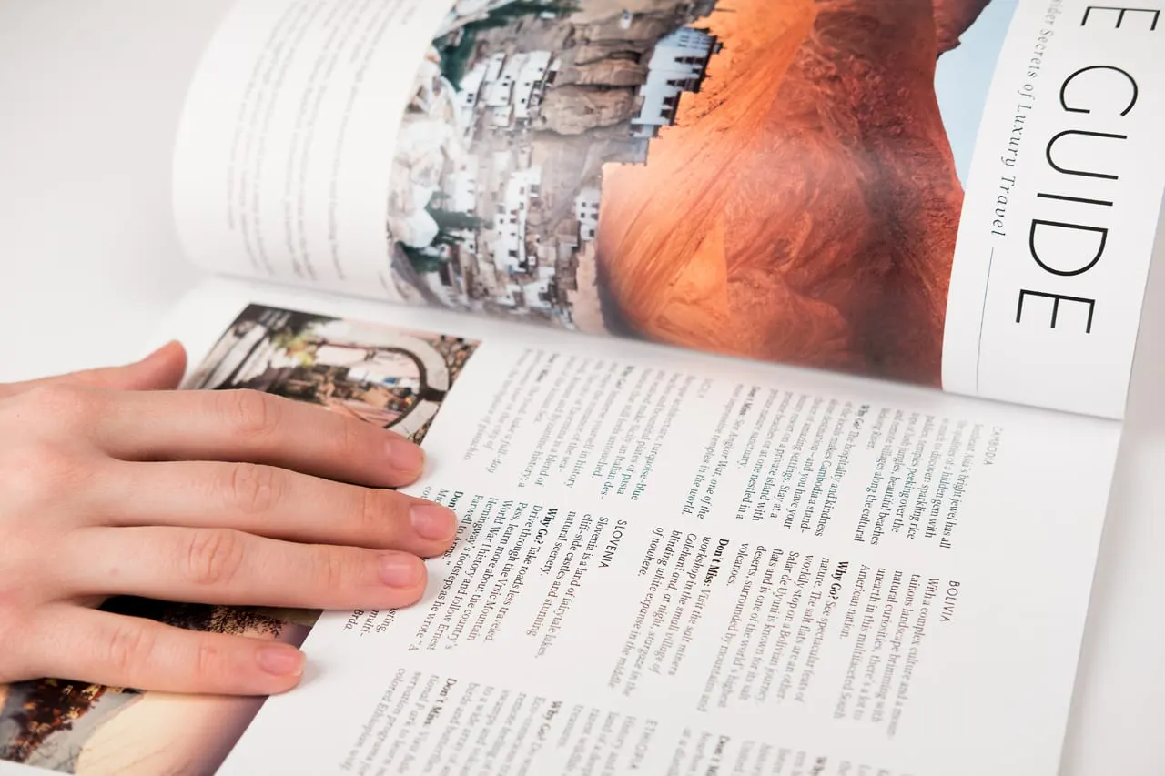 A travel book laying open with a hand on one side and information about Bolivia and Slovenia.