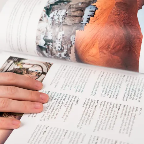 A travel book laying open with a hand on one side and information about Bolivia and Slovenia.