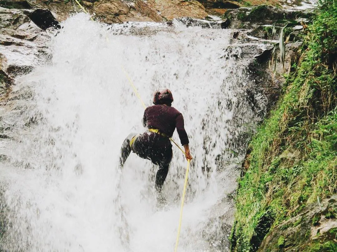 A woman wearing a helmet repelling in waterfall in Antioquia, Colombia.