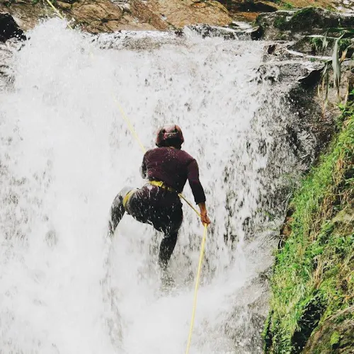 A woman wearing a helmet repelling in waterfall in Antioquia, Colombia.