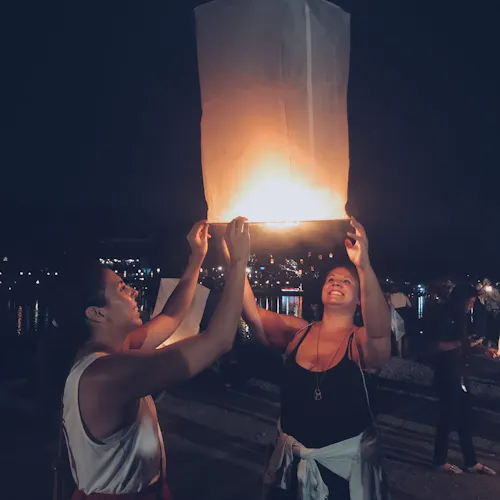 Two women holding a white paper lantern outside at night with other people behind them.