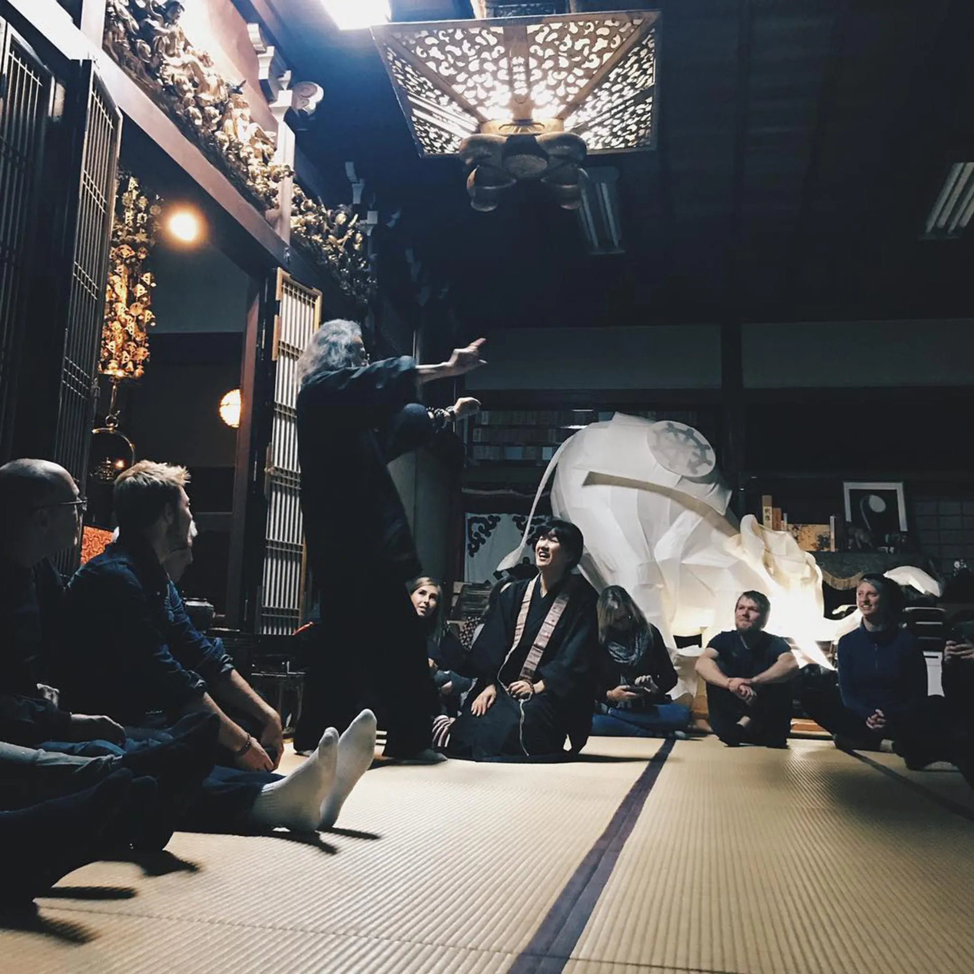 A group of people sitting on the floor in a circle listening to a man speak in the middle in Kyoto, Japan.