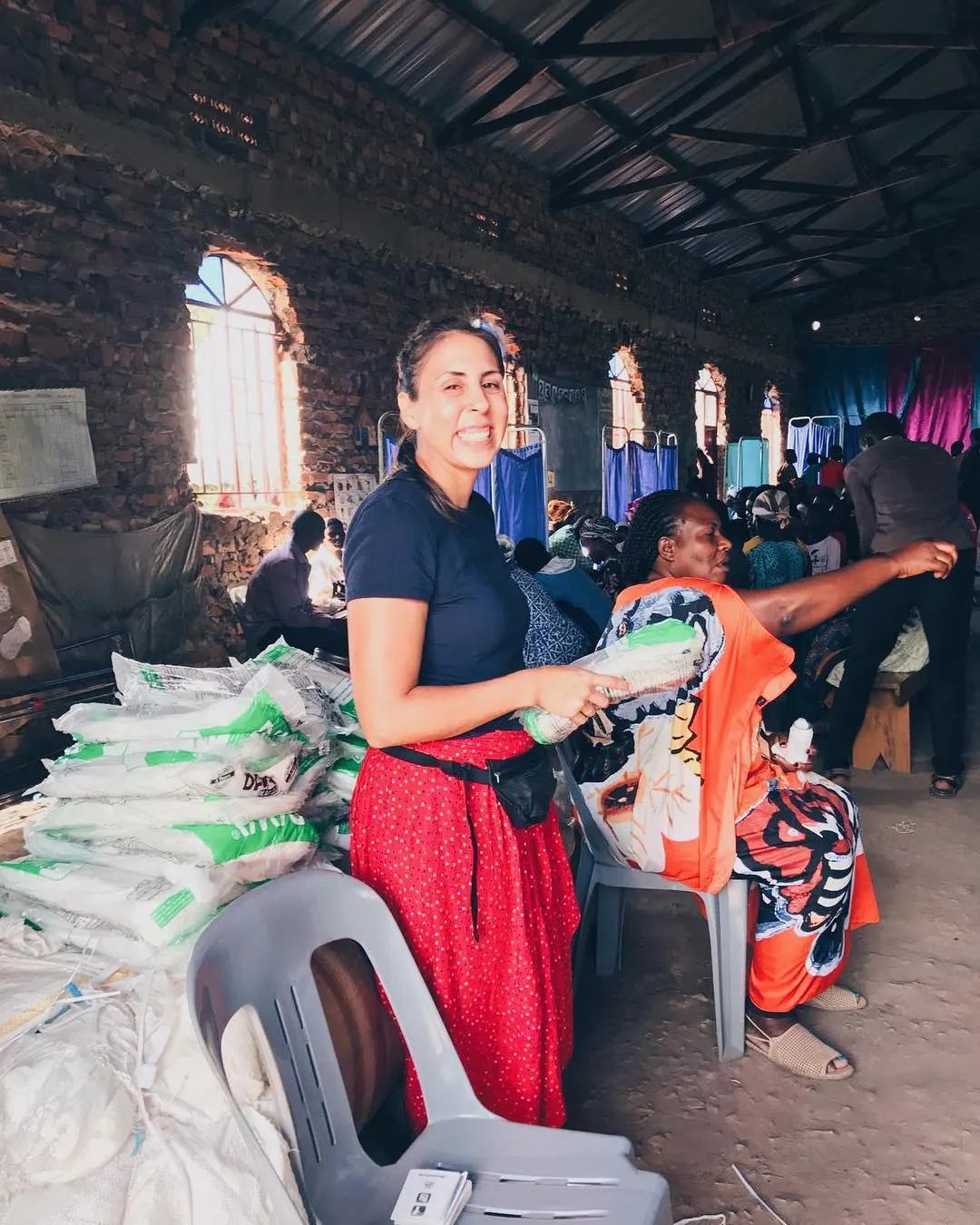 A woman smiling and standing next to a vendor table at an indoor market in Africa.