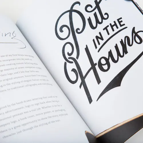 A portfolio book laying open to a print with Put In The Hours in cursive.
