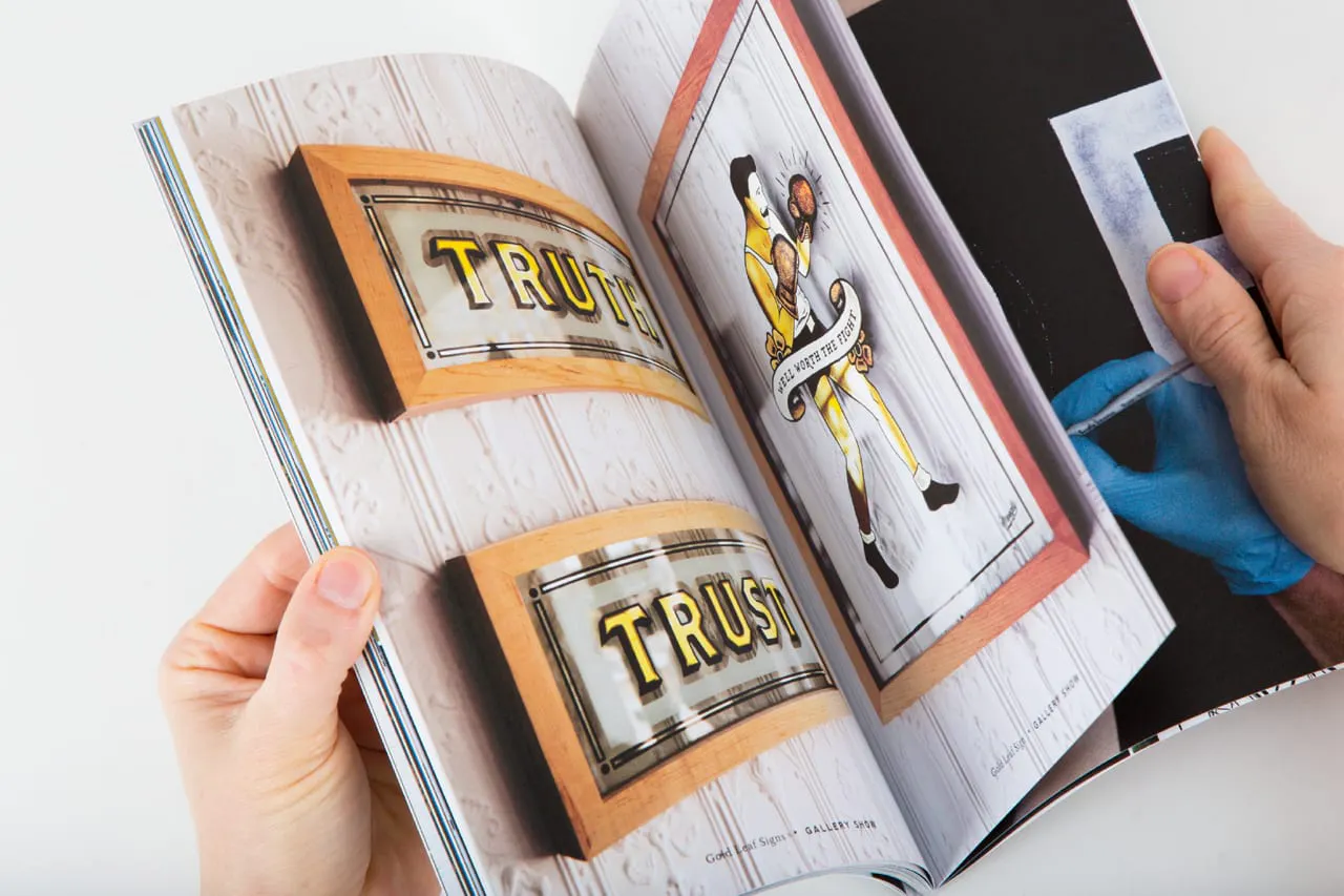A hand flipping through a photography portfolio with images of glass signs inside.