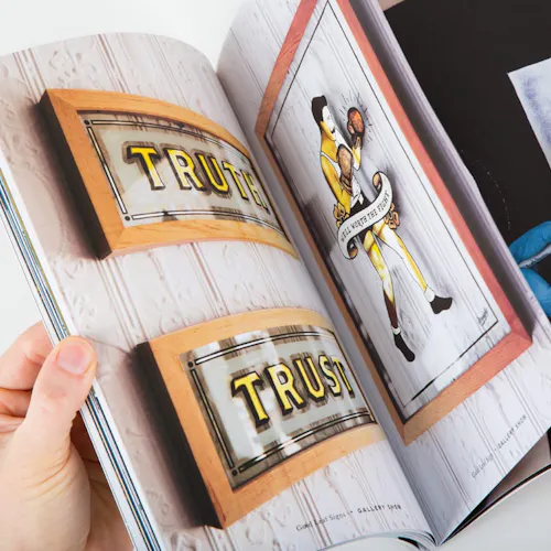 A hand flipping through a photography portfolio with images of glass signs inside.