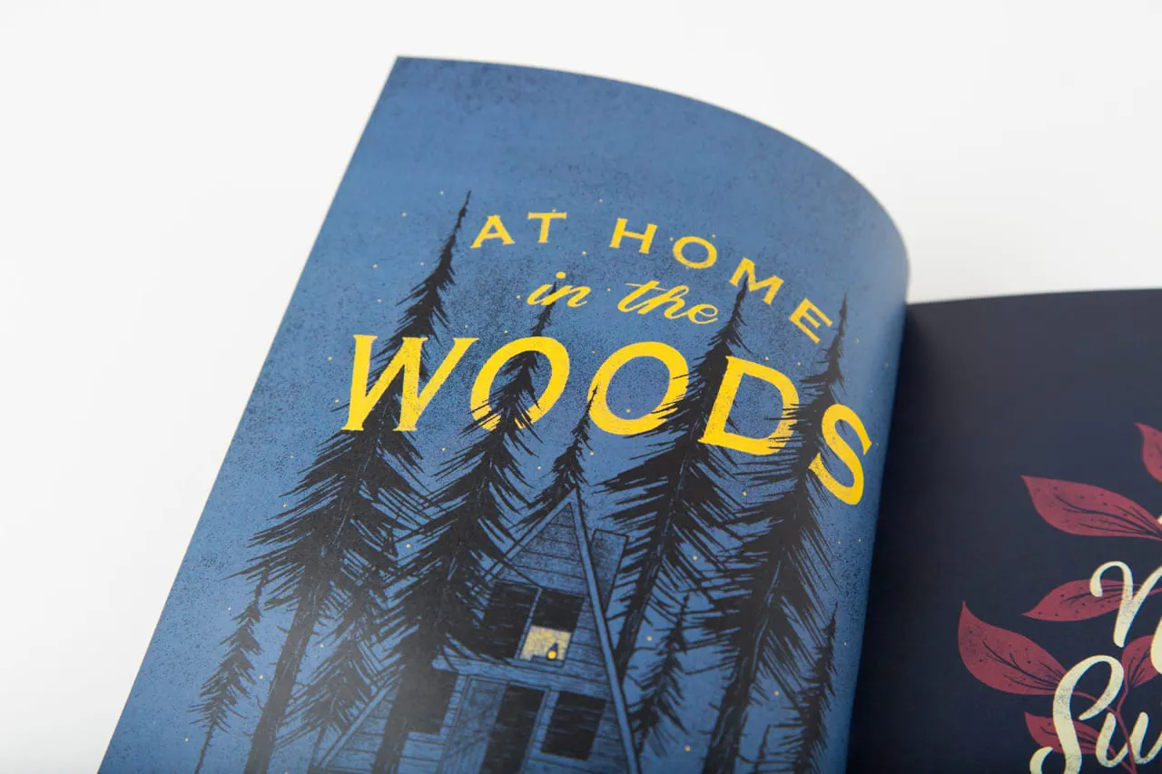 A portfolio book laying open to an illustration of a house in the woods with At Home in the Woods in yellow.