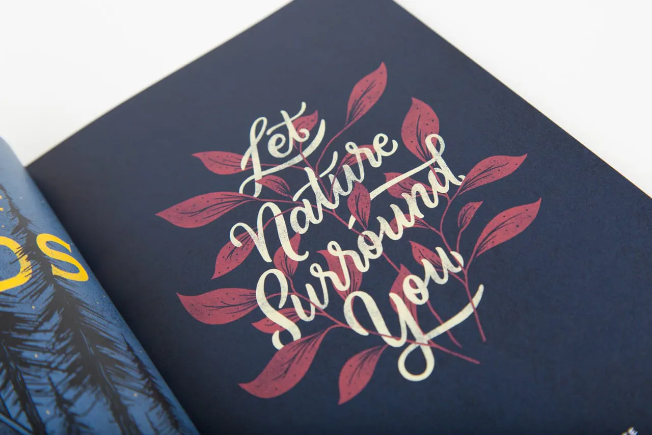 A booklet laying open to a floral illustration with a black background and Let Nature Surround You in cursive.