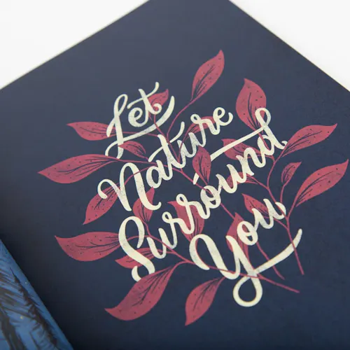 A booklet laying open to a floral illustration with a black background and Let Nature Surround You in cursive.