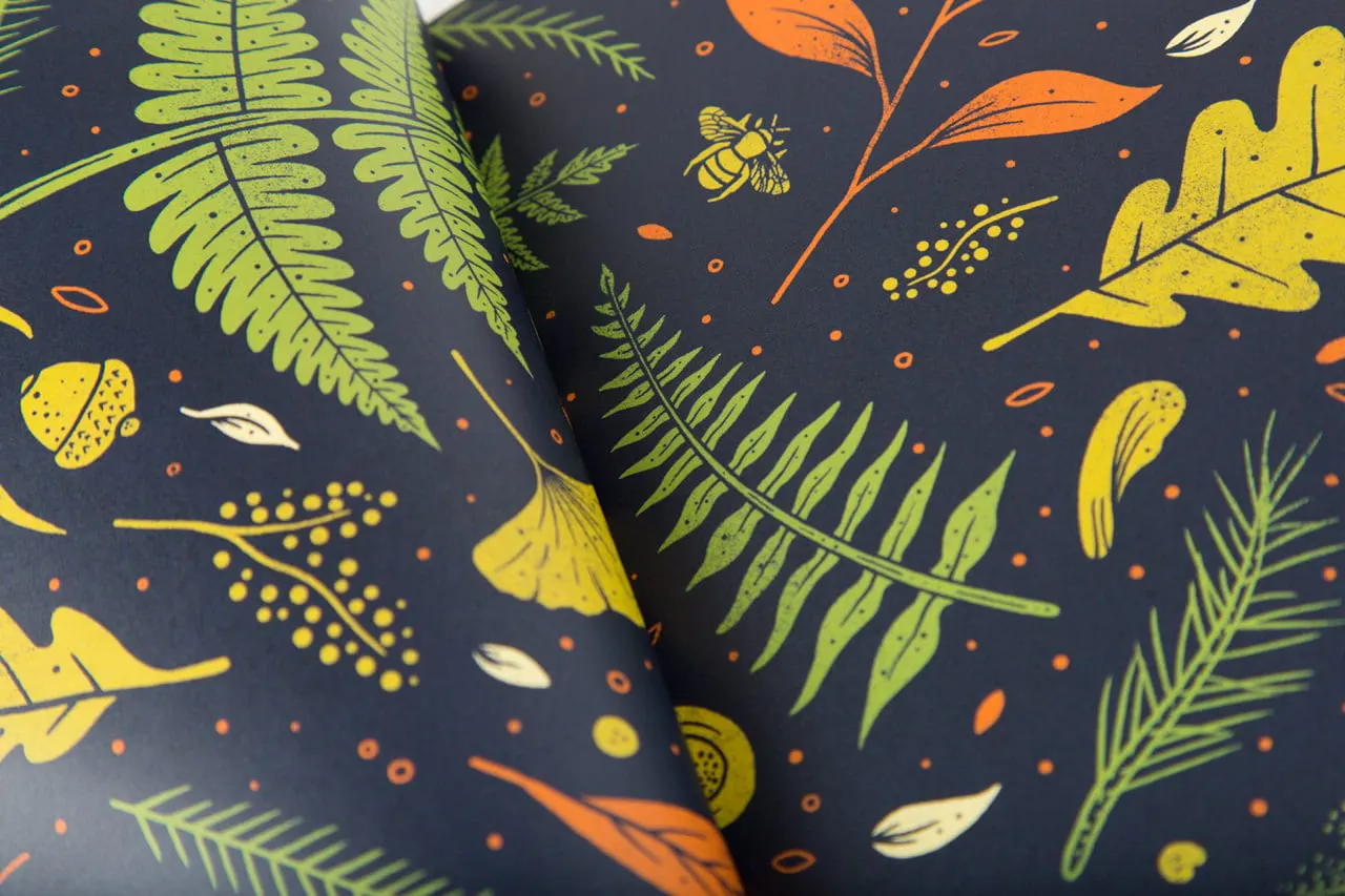 A closeup of two pieces of printed paper with a navy blue background and leaves in green, orange and yellow.