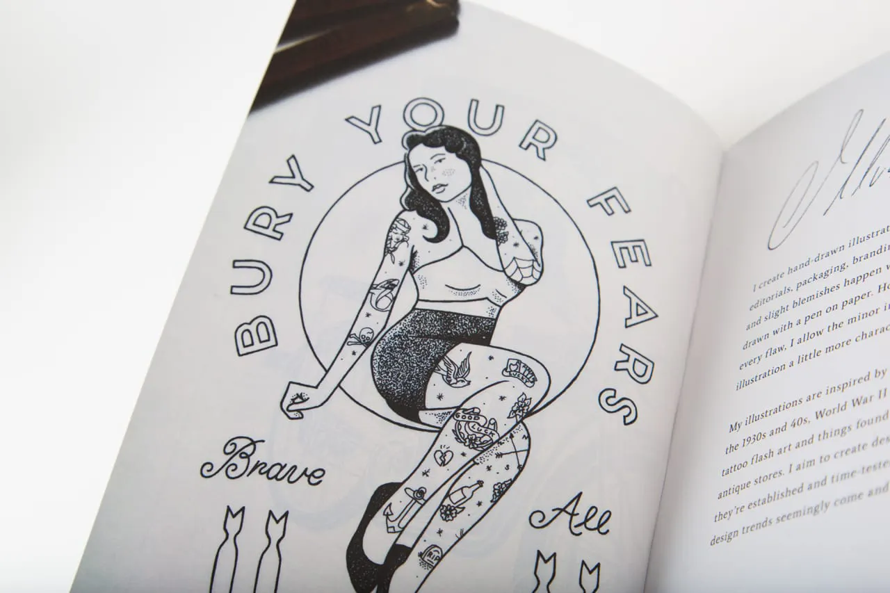 A booklet laying open to a black and white illustration of a girl with tattoos and Bury Your Fears.