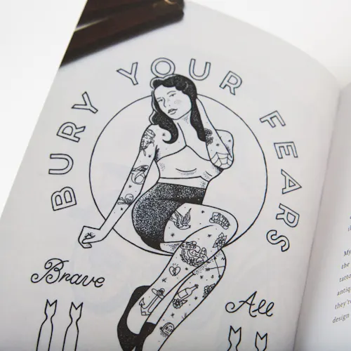 A booklet laying open to a black and white illustration of a girl with tattoos and Bury Your Fears.