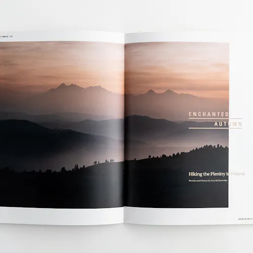 Two hands holding open a visual journal to a landscape of foggy, tree-covered mountains.