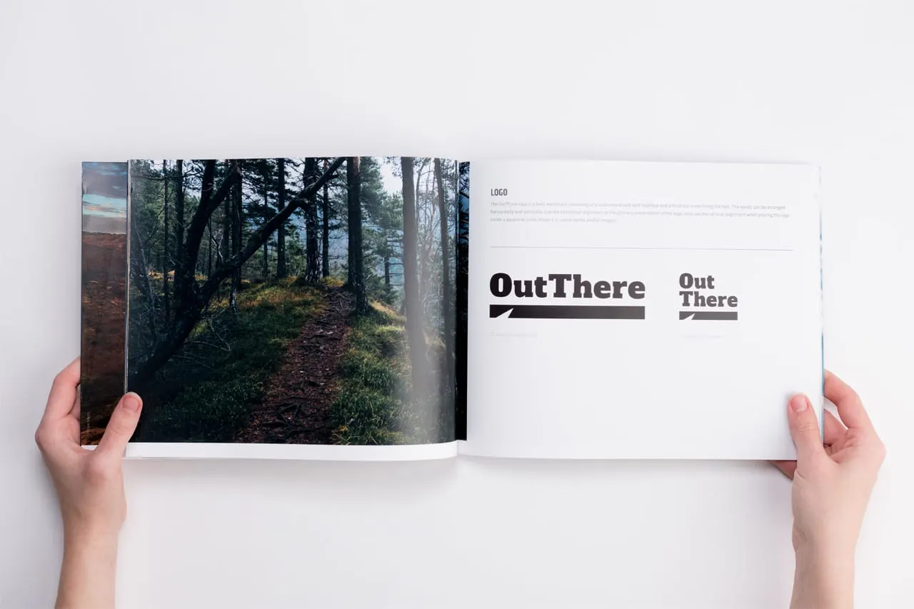 A custom brand manual laying open to a forest and trail scene and Out There in black.
