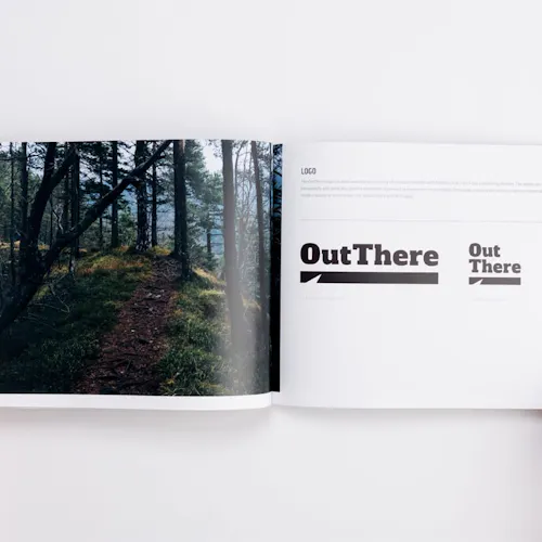 A custom brand manual laying open to a forest and trail scene and Out There in black.
