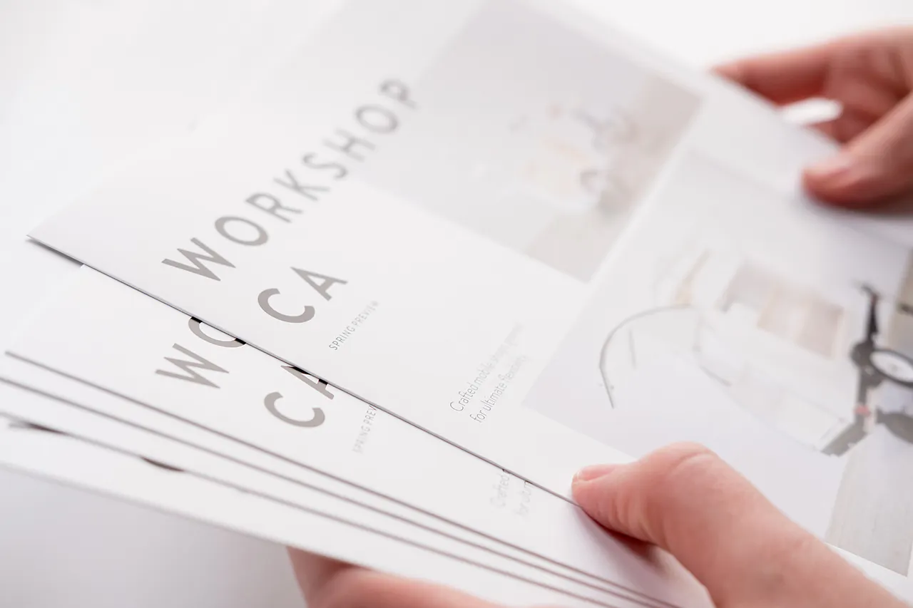 Two hands holding a stack of fanned-out square brochures printed with Workshop CA on the cover.