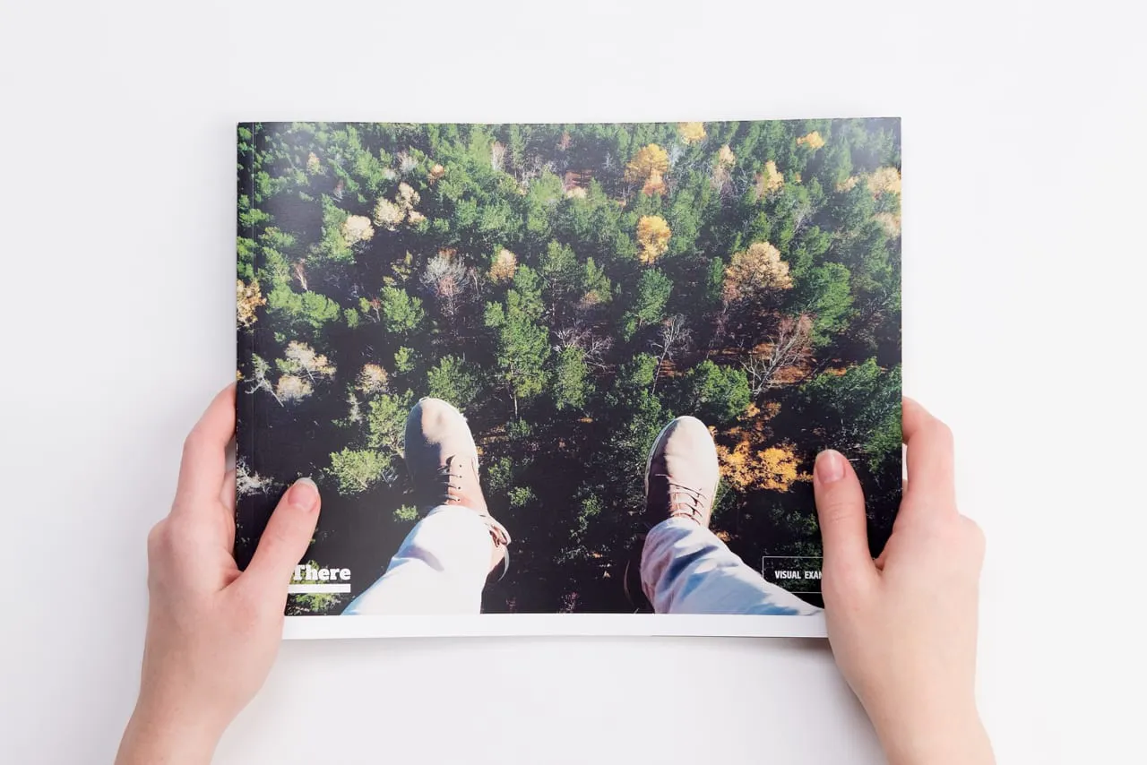 Two hands holding a custom brand manual printed with a forest scene from above on the cover.