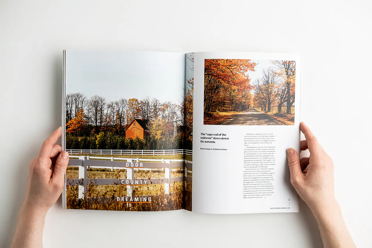 A hand holding open a visual journal to with images of autumn leaves and a farm.