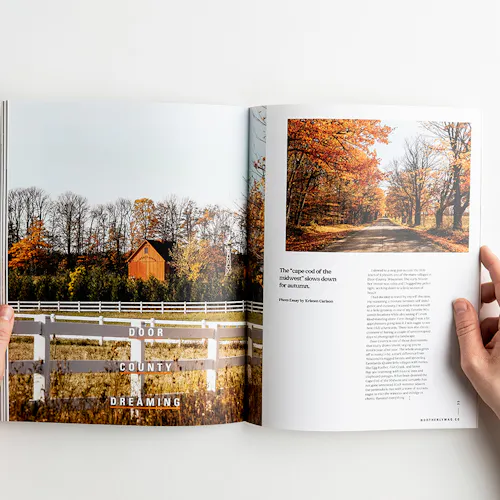 A hand holding open a visual journal to with images of autumn leaves and a farm.