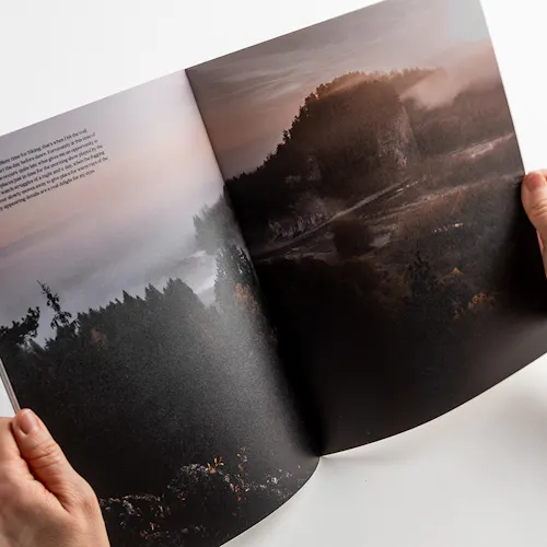 Two hands holding open a visual journal to images of a foggy mountain and lake scene.