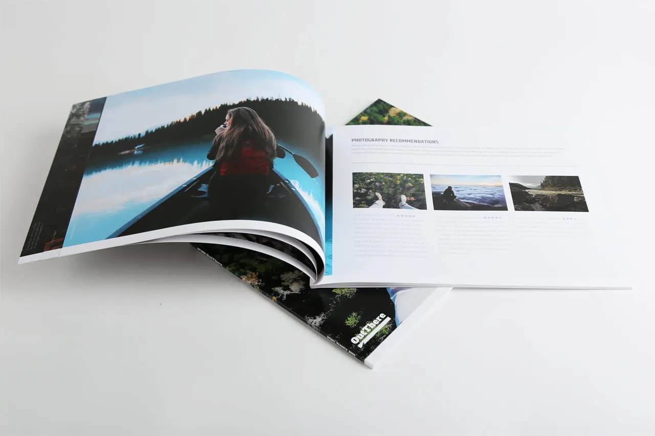 A photography magazine laying on top of another and open to a woman canoeing in a lake surrounded by trees.