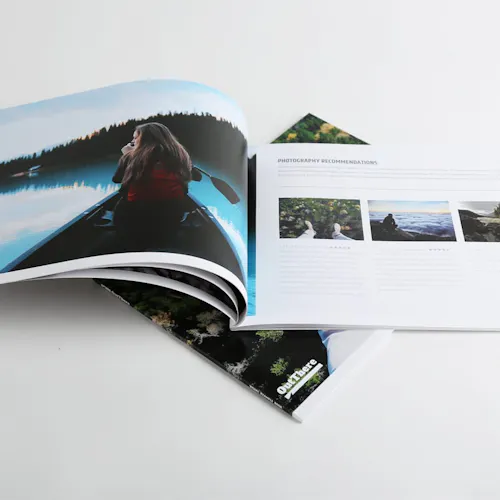 A photography magazine laying on top of another and open to a woman canoeing in a lake surrounded by trees.