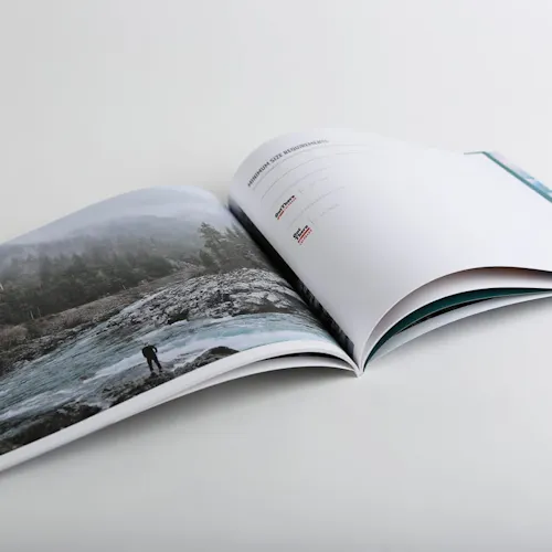 A brand manual laying open to an image of a person standing on the rocky shoreline of a winding river in a forest.