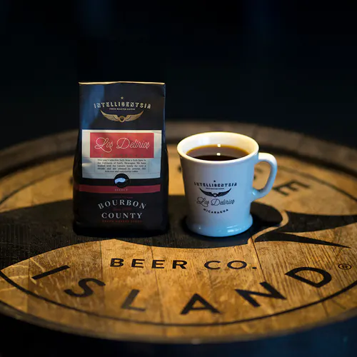 A bag of Intelligentsia coffee beans next to a coffee cup filled with coffee on a wooden barrel.