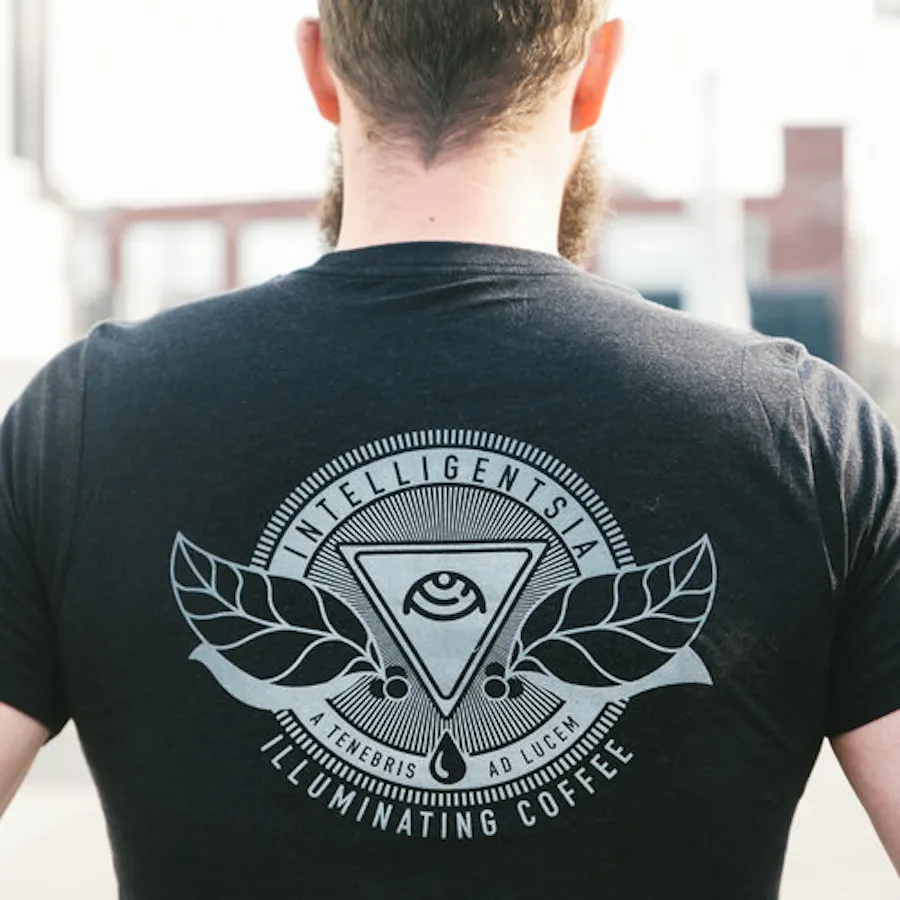 A man wearing a T-shirt printed on the back with Intelligentsia Illuminating Coffee and a leaf logo.