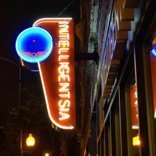 A glowing marquee hanging outside of a building with Intelligentsia in orange and a blue logo.