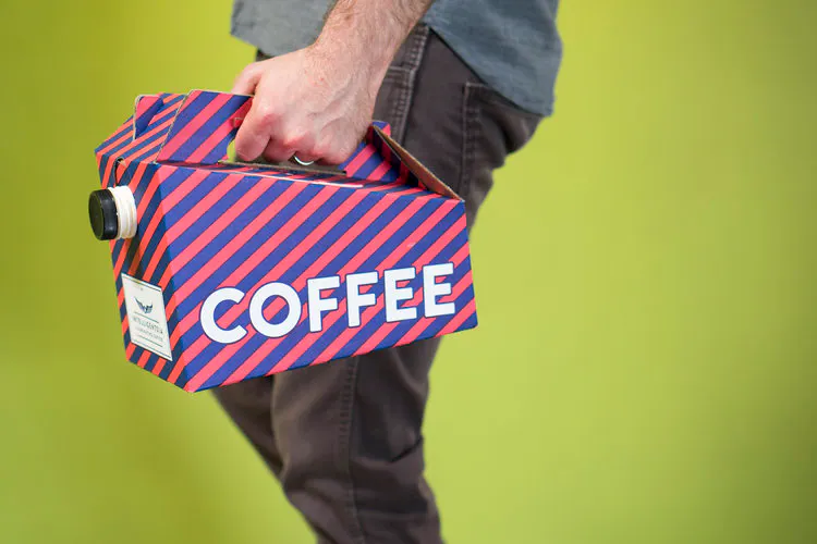 A man standing in profile against a lime green background holding a striped coffee traveler.