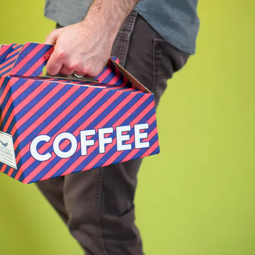 A man standing in profile against a lime green background holding a striped coffee traveler.