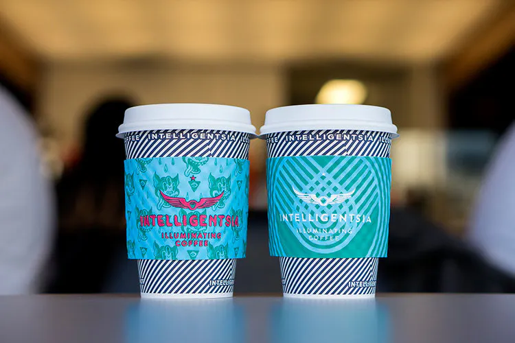 Two coffee cups with a navy blue striped design and coffee sleeves printed with Intelligentsia.