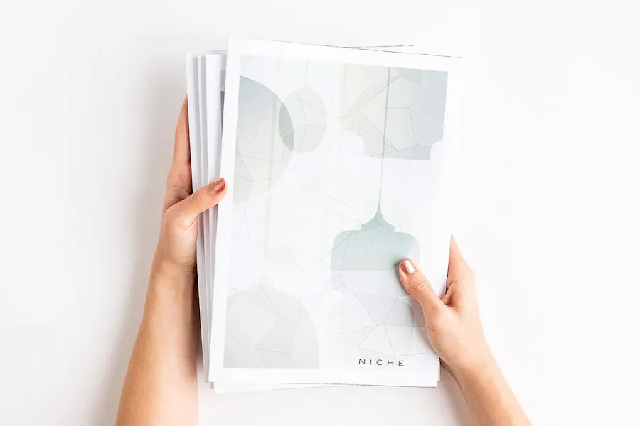 Two hands holding a stack of custom product catalogs with Niche on the cover and an abstract design in pale colors.