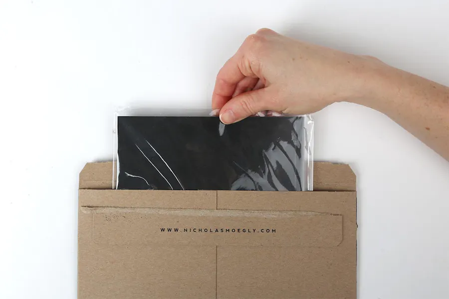 A hand pulling a portfolio with shrink wrap from of its envelope printed with an email address in black letters.