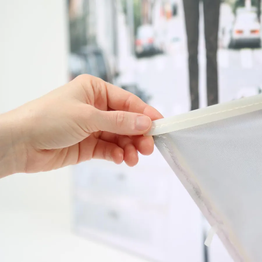 A hand pulling back the corner of a silicone edge graphic with sewn edges on the back.