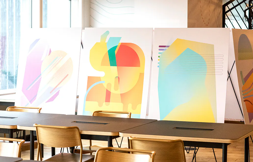 Three custom art prints with abstract geometric designs displayed in front of desks and chairs.