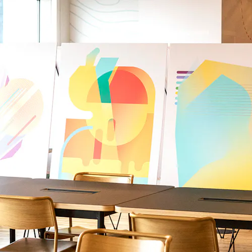 Three custom art prints with abstract geometric designs displayed in front of desks and chairs.