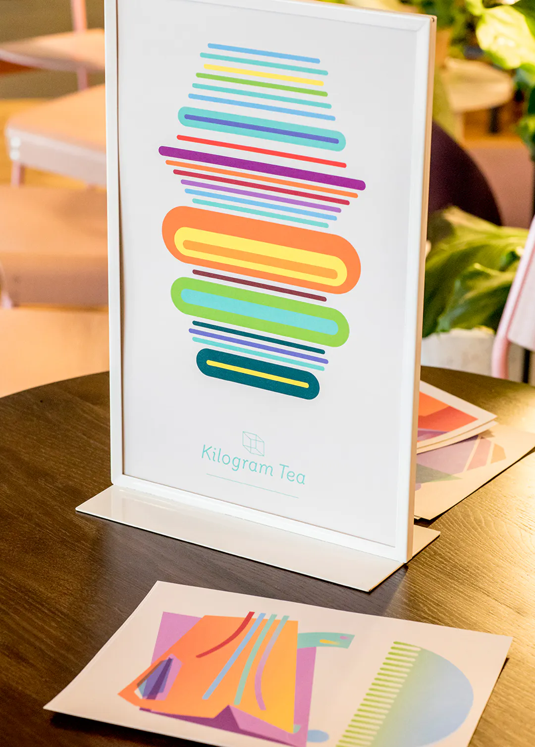 A custom art print in bright orange, blue, pink, purple and yellow in a white free-standing frame sitting on a table.