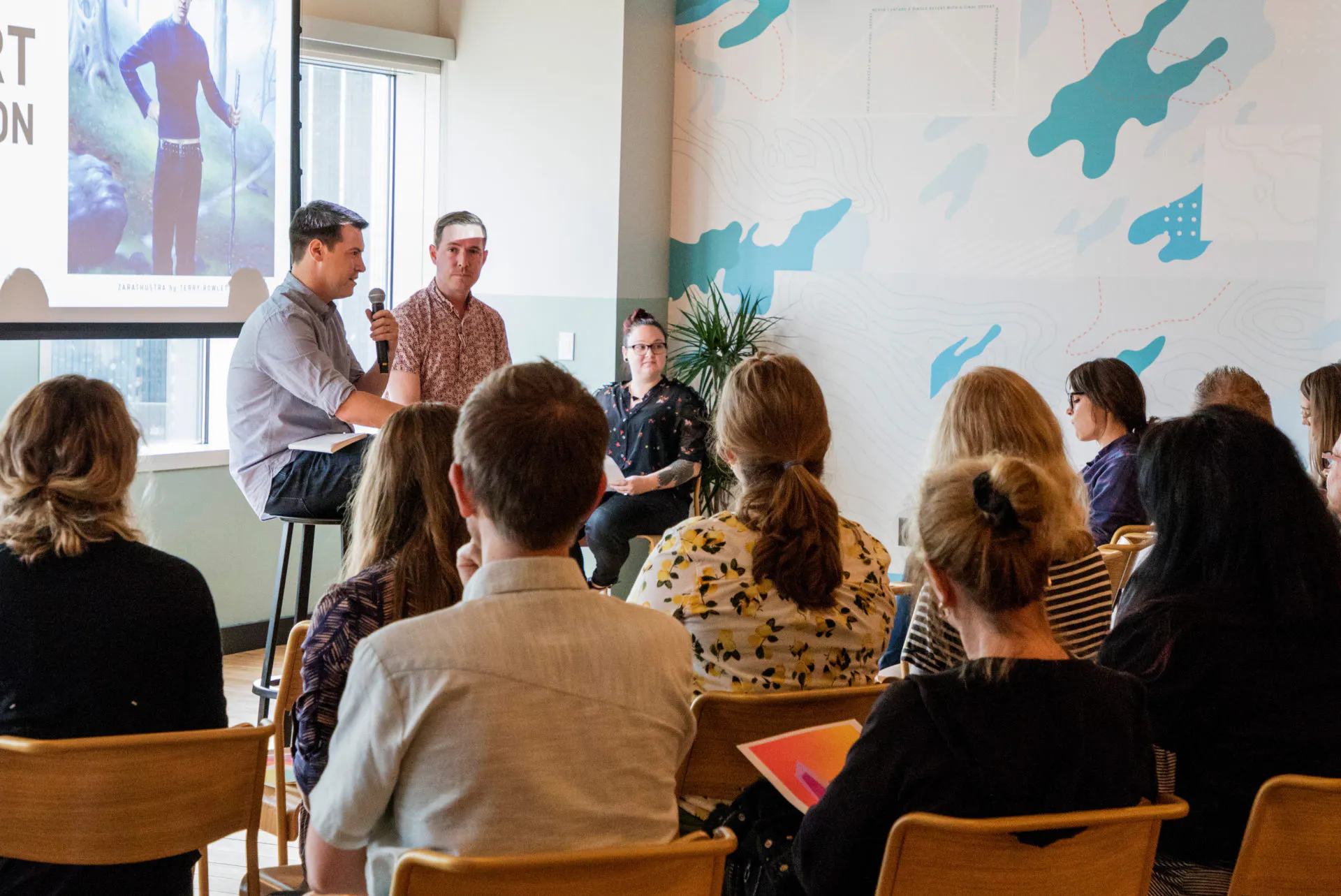 Two men holding microphones and sitting in front of an audience during a presentation.